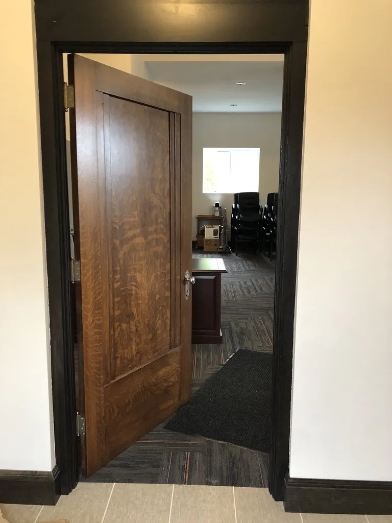 A restored quartersawn oak door opening into a carpeted meeting room