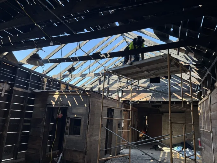 A worker on scaffolding inside the depot, with the old roof boards removed and blue sky showing through the rafters