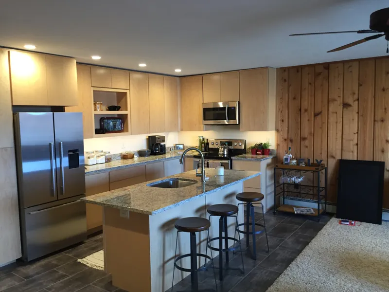 A kitchen with a granite island, stools and a cedar wall