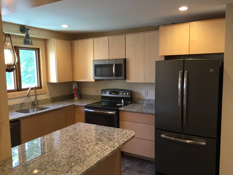 A kitchen with maple cabinets, granite counters and dark appliances