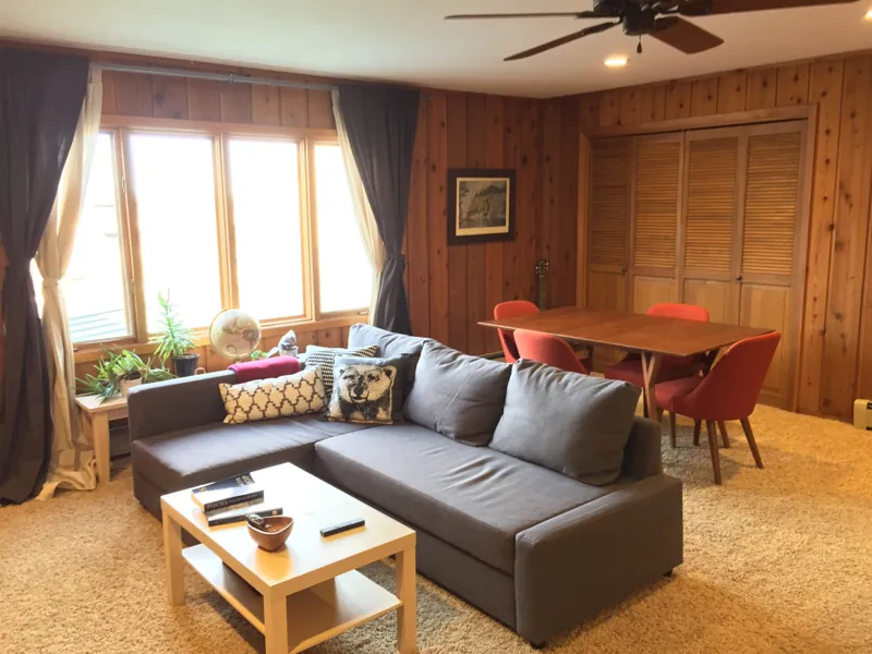 A cedar-paneled living room with a sectional and dining table