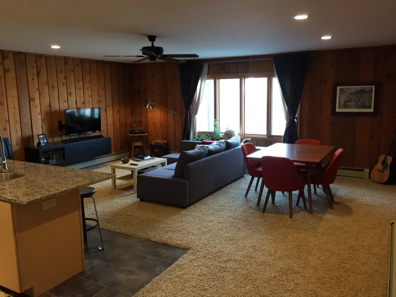 A cedar-paneled living room with a dining table by the windows