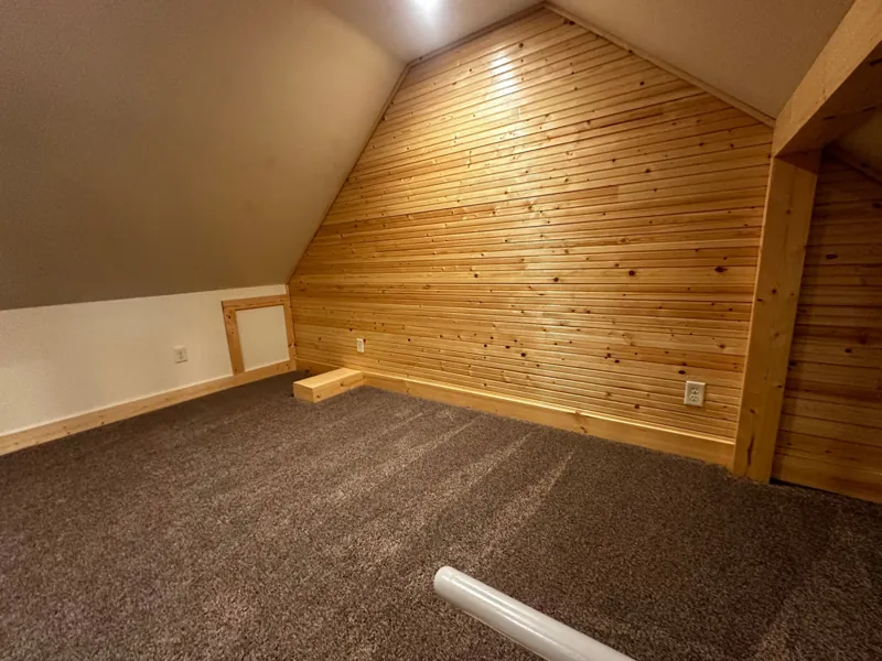 A carpeted loft room with a cedar accent wall