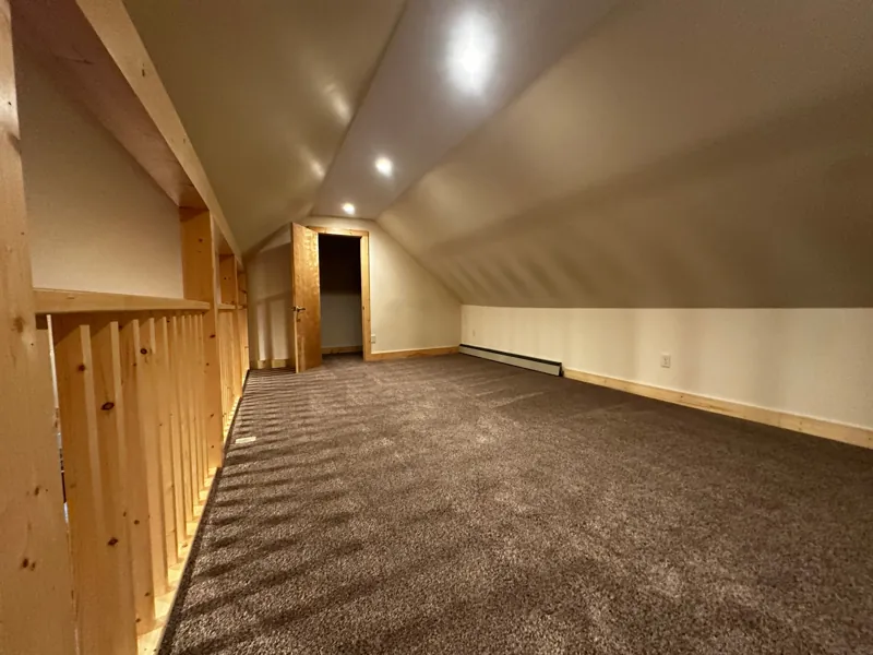 A long carpeted loft under the sloped ceiling with a pine railing