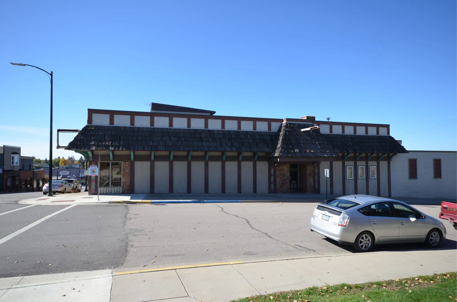 The building with a shingled mansard roof and boarded panels along the side street