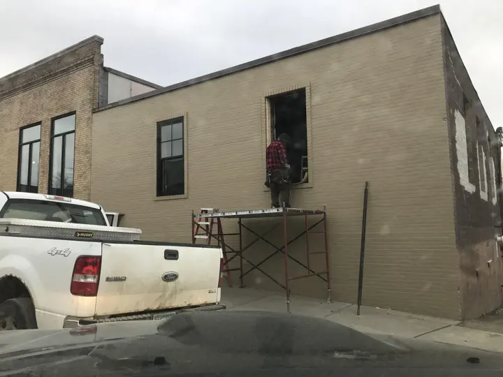 A worker on scaffolding installing a window in the rear brick addition