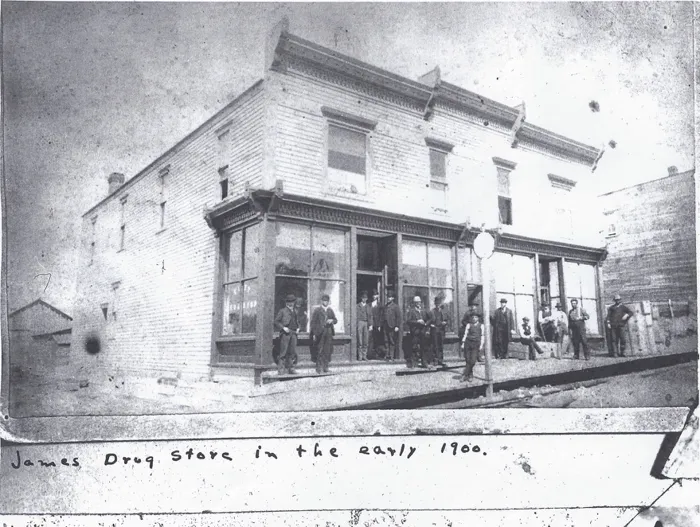 The white two-story James Drug Store in the early 1900s with a group of men out front