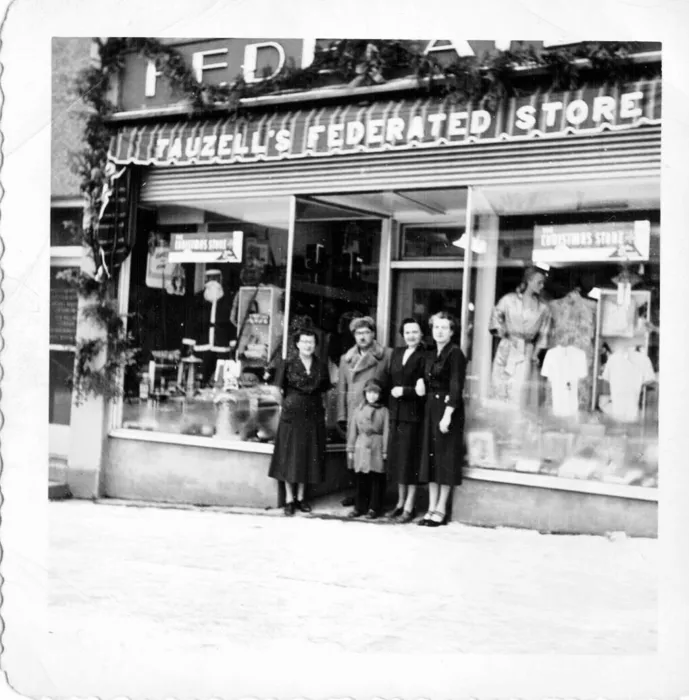 Four women, a man and a child standing in front of Tauzell’s Federated Store decorated for Christmas