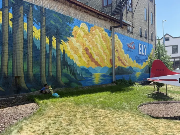 A toddler playing on the lawn in front of the forest and lake mural
