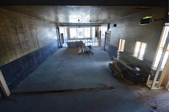 The long interior looking toward the street windows with lumber stacked on the floor