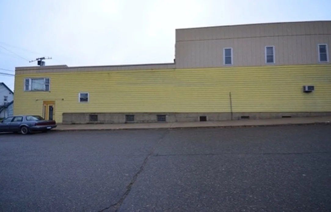 The side of the Salerno Building before renovation with yellow lap siding