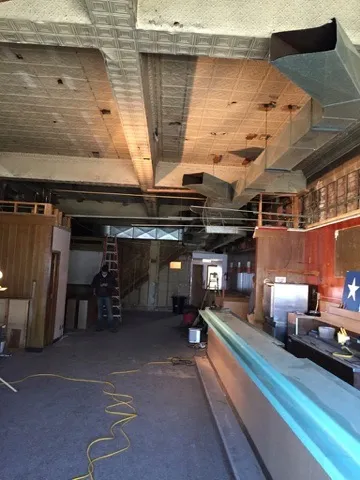 The long bar room with ceiling tiles removed and ductwork exposed beneath the tin